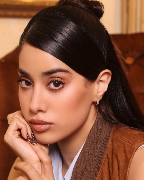 Close-up portrait of a woman with glossy dark hair, subtle makeup, and a thoughtful expression resting her chin on her hand indoors.